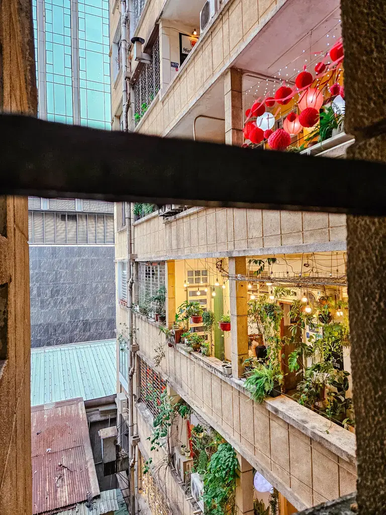 2025胡志明市旅遊指南|從行前準備到在地美食景點,一篇搞懂自由行大小事 胡志明市咖啡公寓內部視角,呈現改造為咖啡廳或商店的公寓陽台,掛著燈飾並有綠色植物裝飾。 (Interior view of The Cafe Apartment in Ho Chi Minh City, showing apartment balconies converted into cafes or shops, decorated with lights and green plants.)