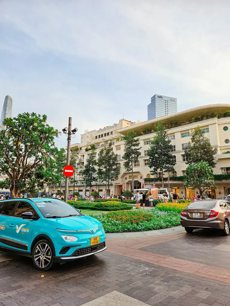 2025胡志明市旅遊指南|從行前準備到在地美食景點,一篇搞懂自由行大小事 胡志明市 Rex Hotel 前方的街道景象,有一輛薄荷綠色計程車和花圃