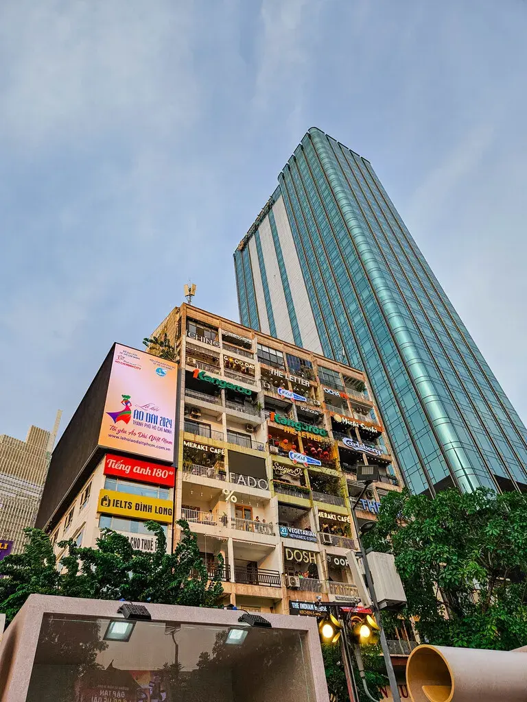 2025胡志明市旅遊指南|從行前準備到在地美食景點,一篇搞懂自由行大小事 胡志明市景點:咖啡公寓建築的外觀,老舊公寓每層樓都有商店招牌,旁邊是現代高樓。 (Facade of The Cafe Apartment building in Ho Chi Minh City, showing various shop signs on each floor of the old apartment block, next to a modern high-rise.)