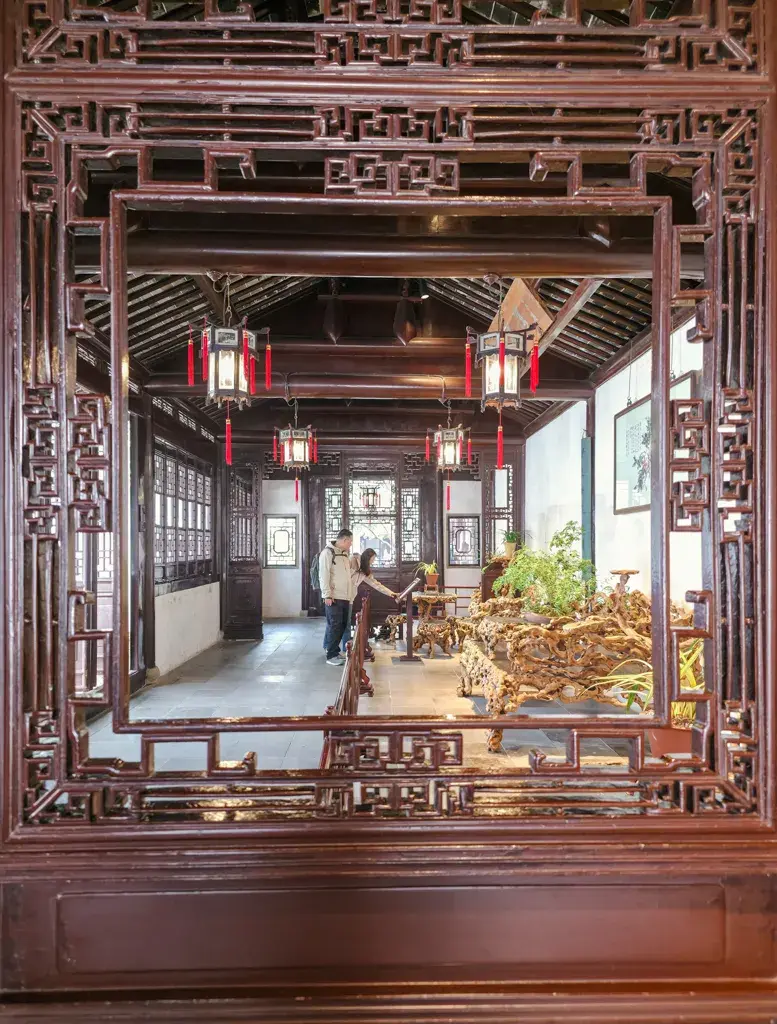 2026 蘇州旅遊攻略|5日遊深度自由行:避開人潮的園林路線、美食、住宿、交通一次搞懂 蘇州滄浪亭古典園林的精緻框景美學:透過木質花窗望向懸掛紅燈籠的室內空間與傳統根雕家具,展現世界遺產園林的建築細節。