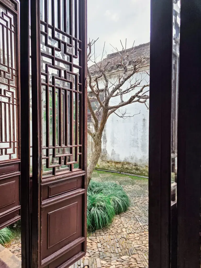 2026 蘇州旅遊攻略|5日遊深度自由行:避開人潮的園林路線、美食、住宿、交通一次搞懂 蘇州景點「滄浪亭」古典園林的室內框景:透過精緻的雕花木門,望向庭院中的蒼勁古樹與白牆,展現世界遺產園林的建築細節。