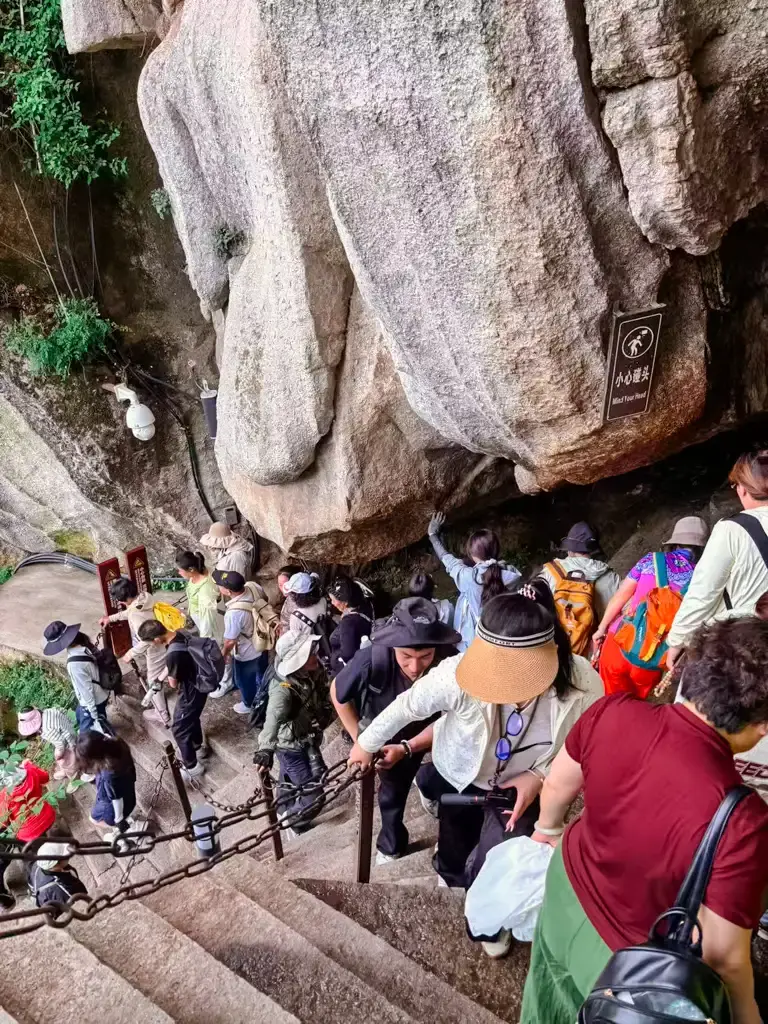 中國華山景區內狹窄且充滿挑戰的石階通道,遊客需小心低頭通過巨石