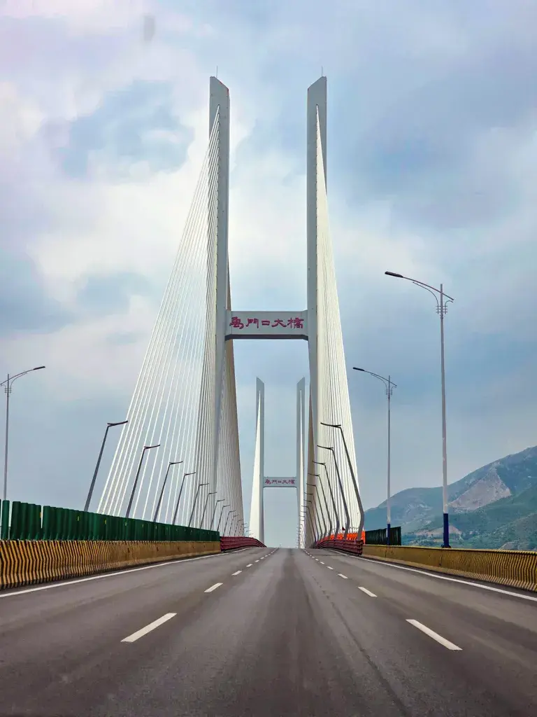 大陸自駕遊行經跨越黃河兩岸的禹門口大橋(禹門口黃河大橋)實拍,畫面上呈現第一人稱筆直公路的行車視角,主體為宏偉對稱的白色斜張橋塔與鋼索結構,此橋連接了山西河津與陝西韓城。
