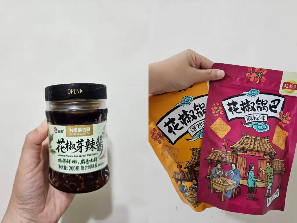 陝西韓城古城自由行必買伴手禮推薦:手持特產「為康麻香廚花椒芽辣醬」玻璃罐,以及「武老三花椒鍋巴」爆辣味與麻辣味包裝袋,展現當地獨特的花椒飲食文化。