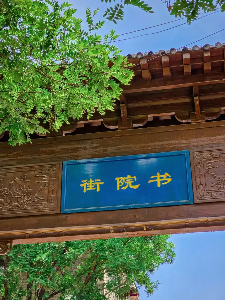 韓城古城「書院街」復古木造門樓牌匾特寫,藍底金字的木質匾額在翠綠樹葉與古典木構屋簷的襯託下,顯得充滿書香氣息。